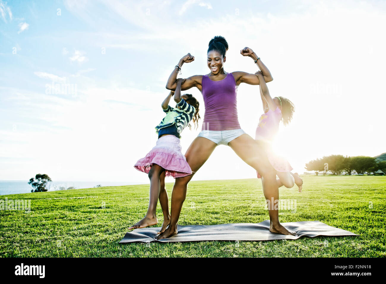 Woman lifting children with biceps in park Stock Photo