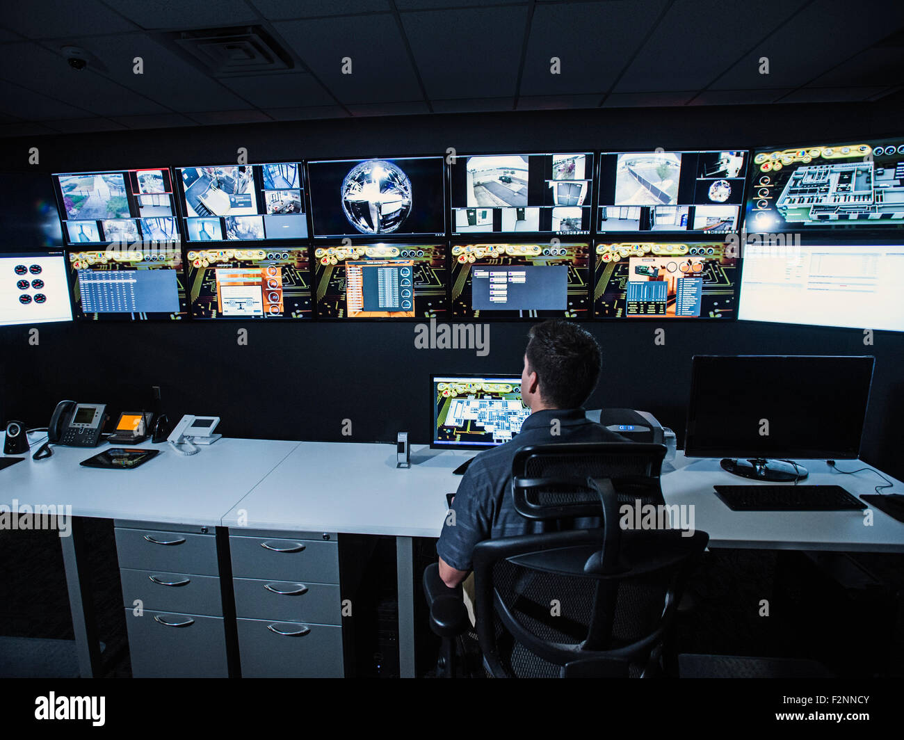 Hispanic security guard watching monitors in control room Stock Photo