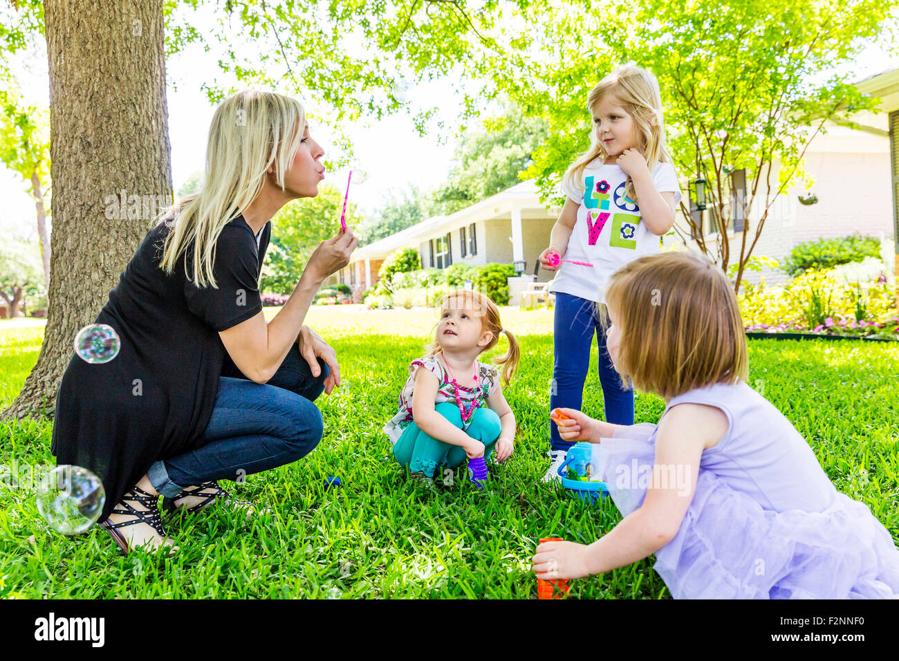 Caucasian mother and daughters blowing bubbles in backyard Stock Photo