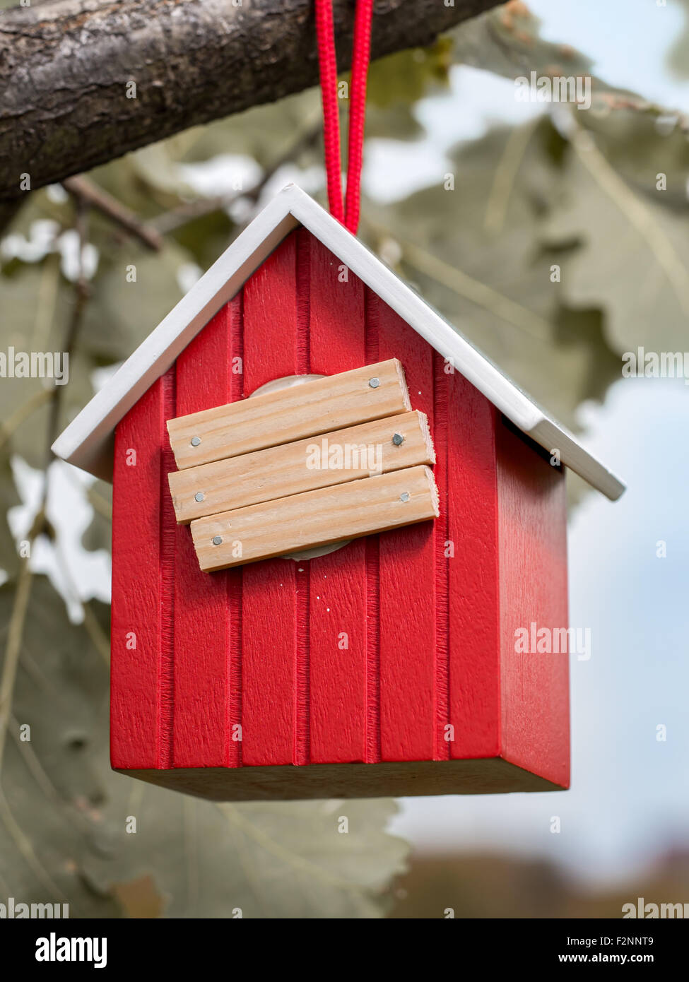 Wooden red birdhouse hanging on tree branch with entry hole covered with planks Stock Photo