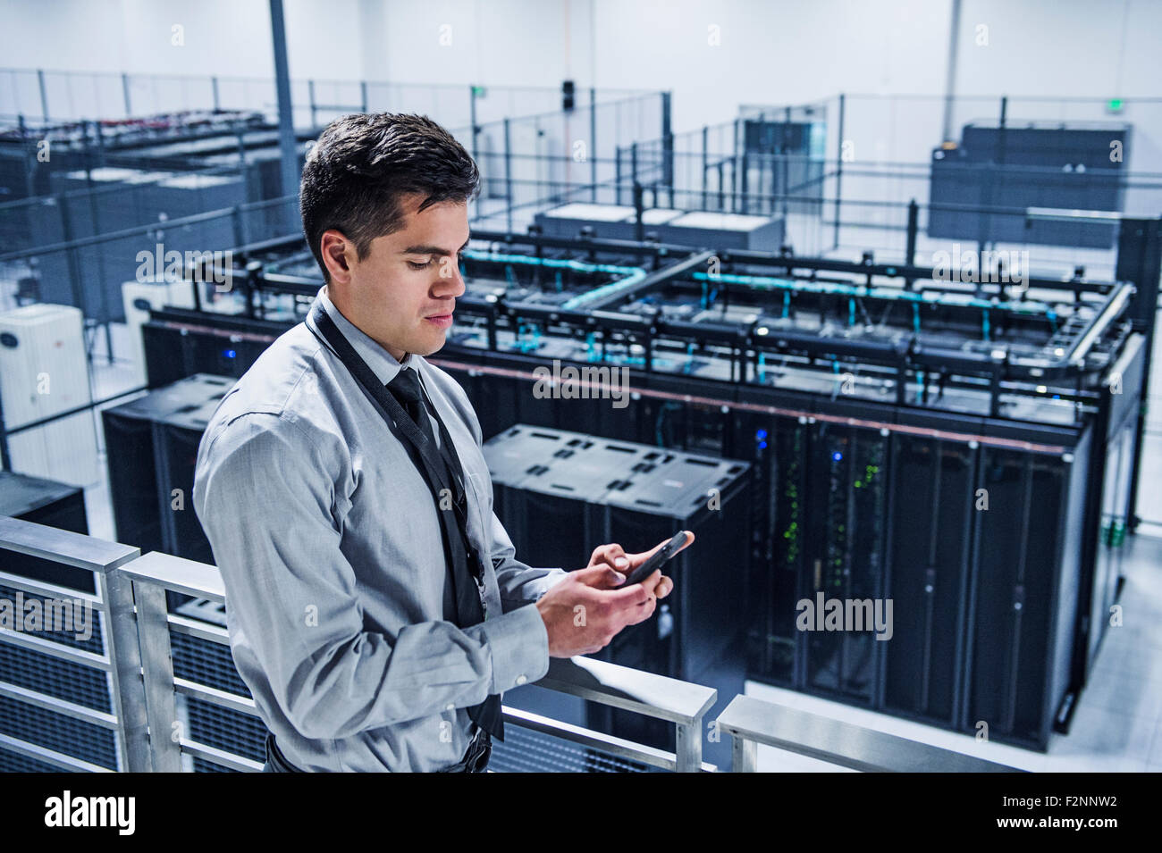 Hispanic businessman using cell phone on balcony over server room Stock