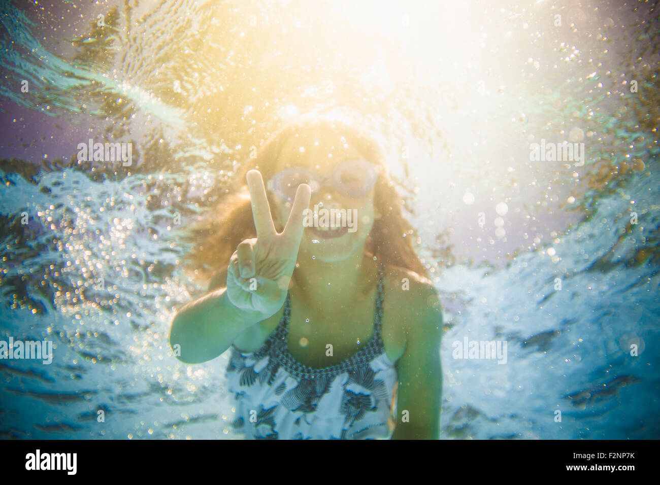 Caucasian girl swimming underwater gesturing peace sign Stock Photo