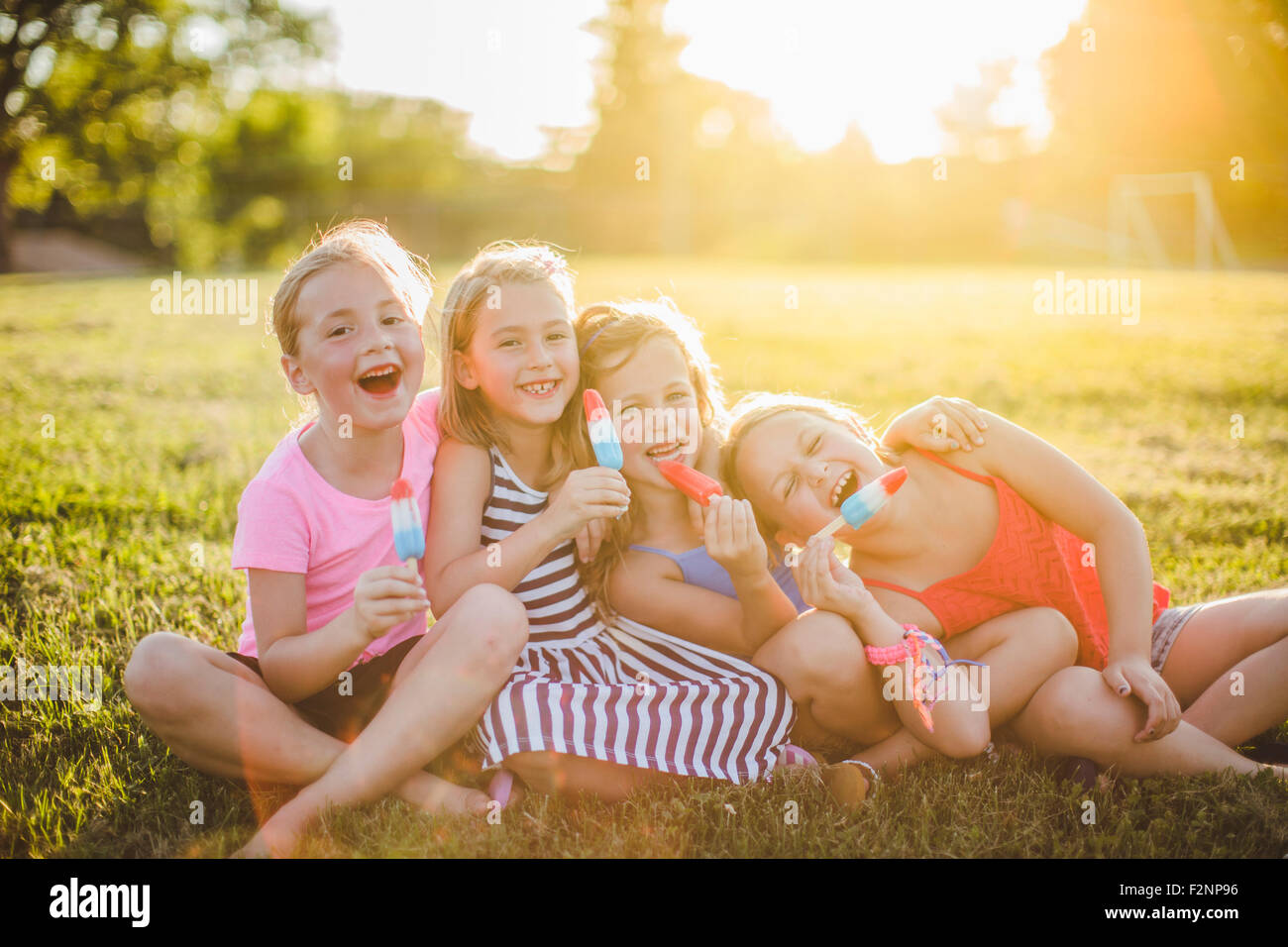 Girls eating flavored ice in sunny field Stock Photo