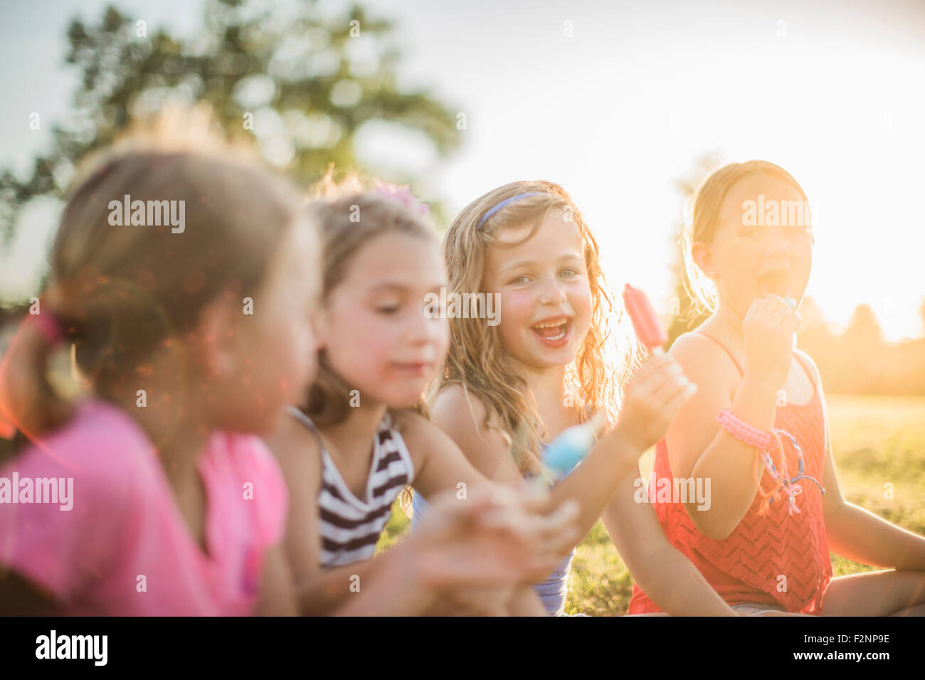 Girls eating flavored ice in sunny field Stock Photo