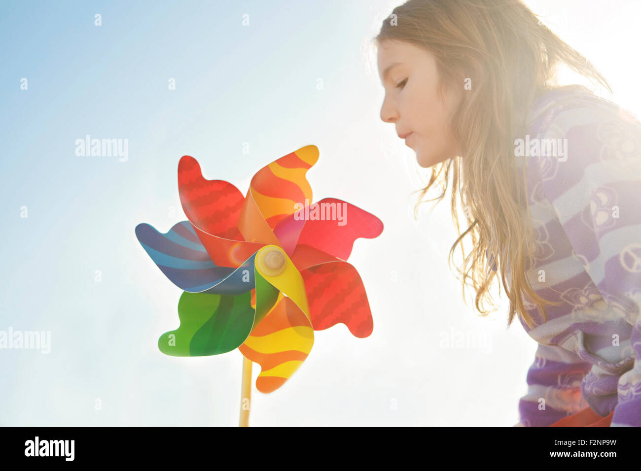 Caucasian girl playing with pinwheel under blue sky Stock Photo