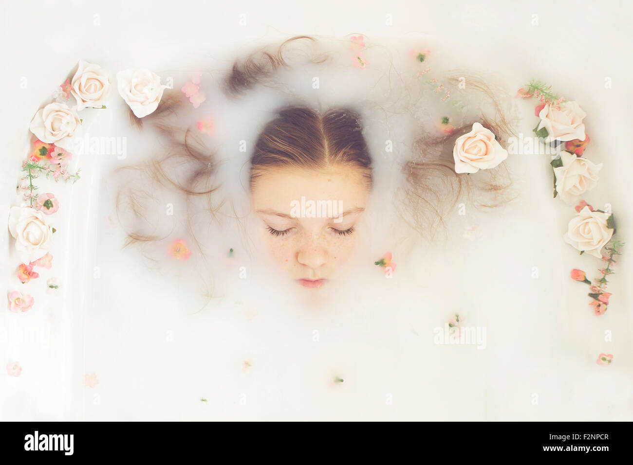 Caucasian teenage girl floating in milk bath with flowers Stock Photo