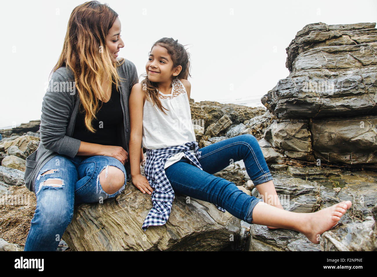 Hispanic mother and daughter sitting at tide pools Stock Photo