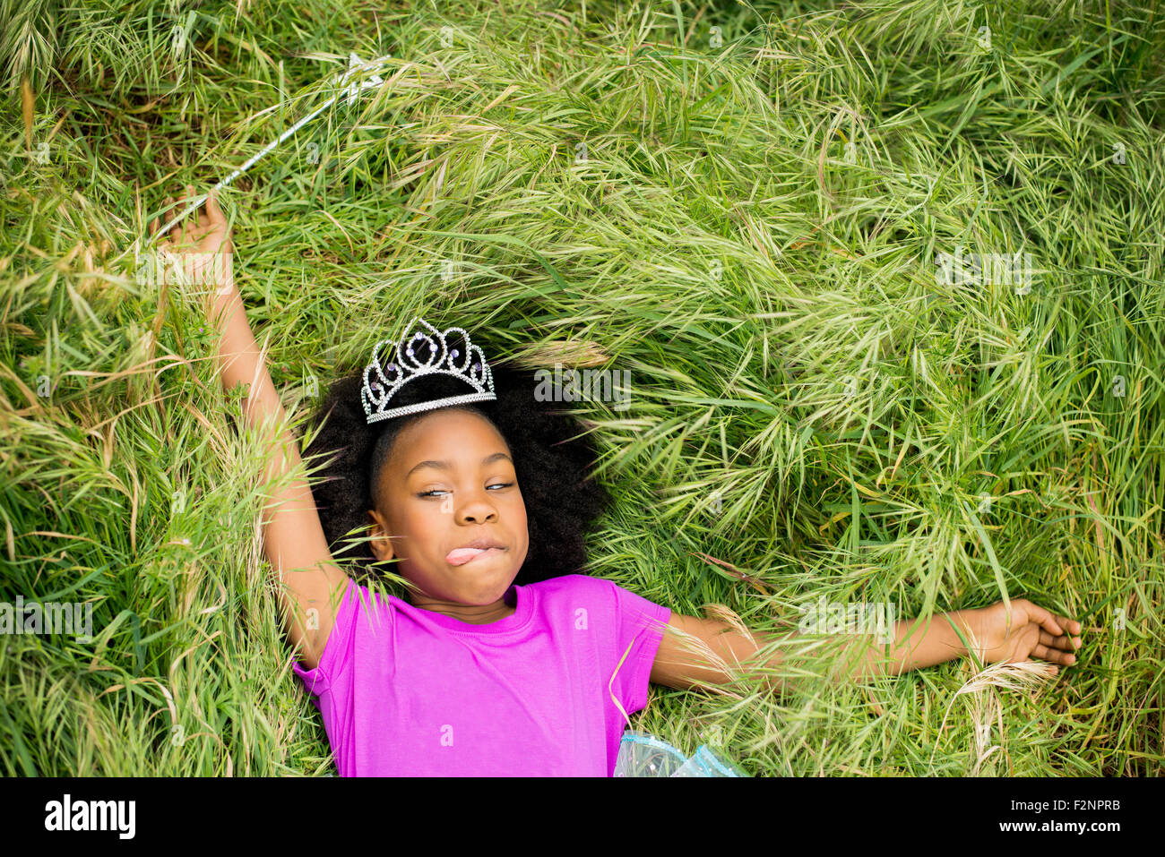 Black girl in princess tiara laying in grass Stock Photo