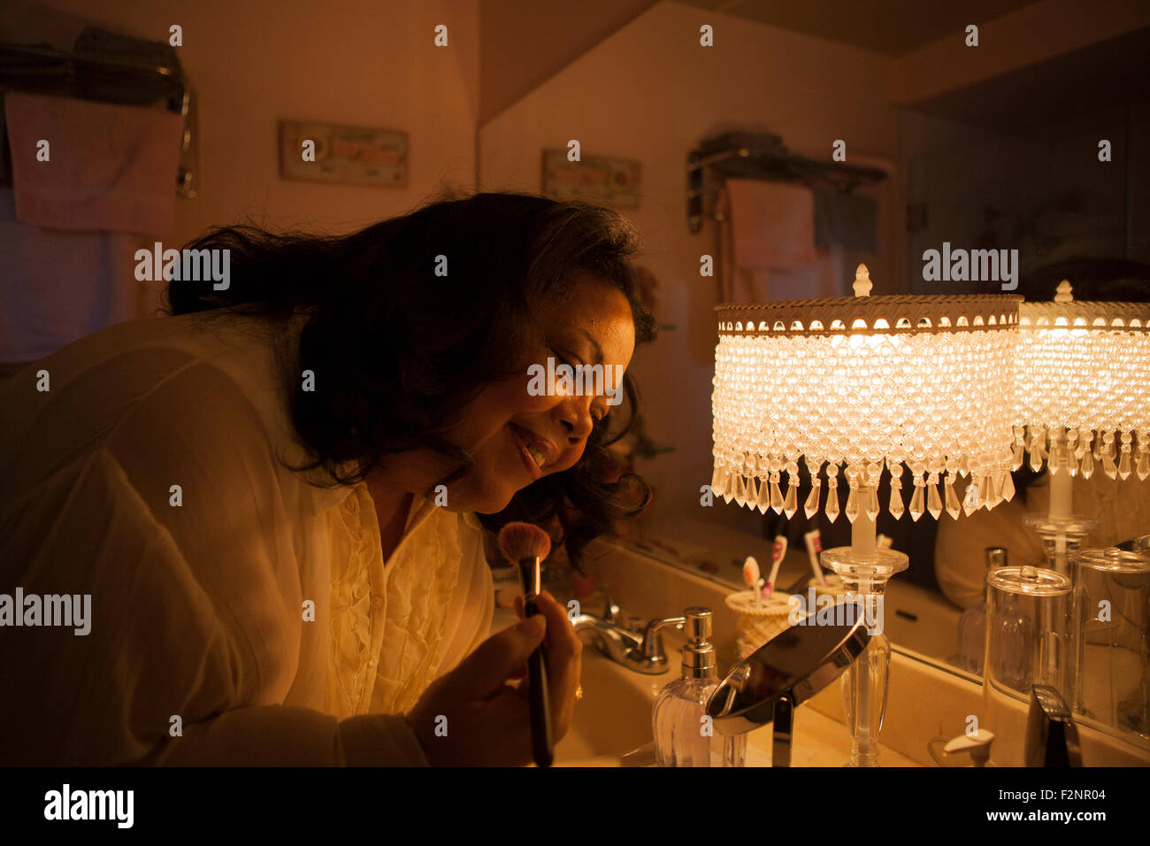 Woman applying makeup in bathroom mirror Stock Photo