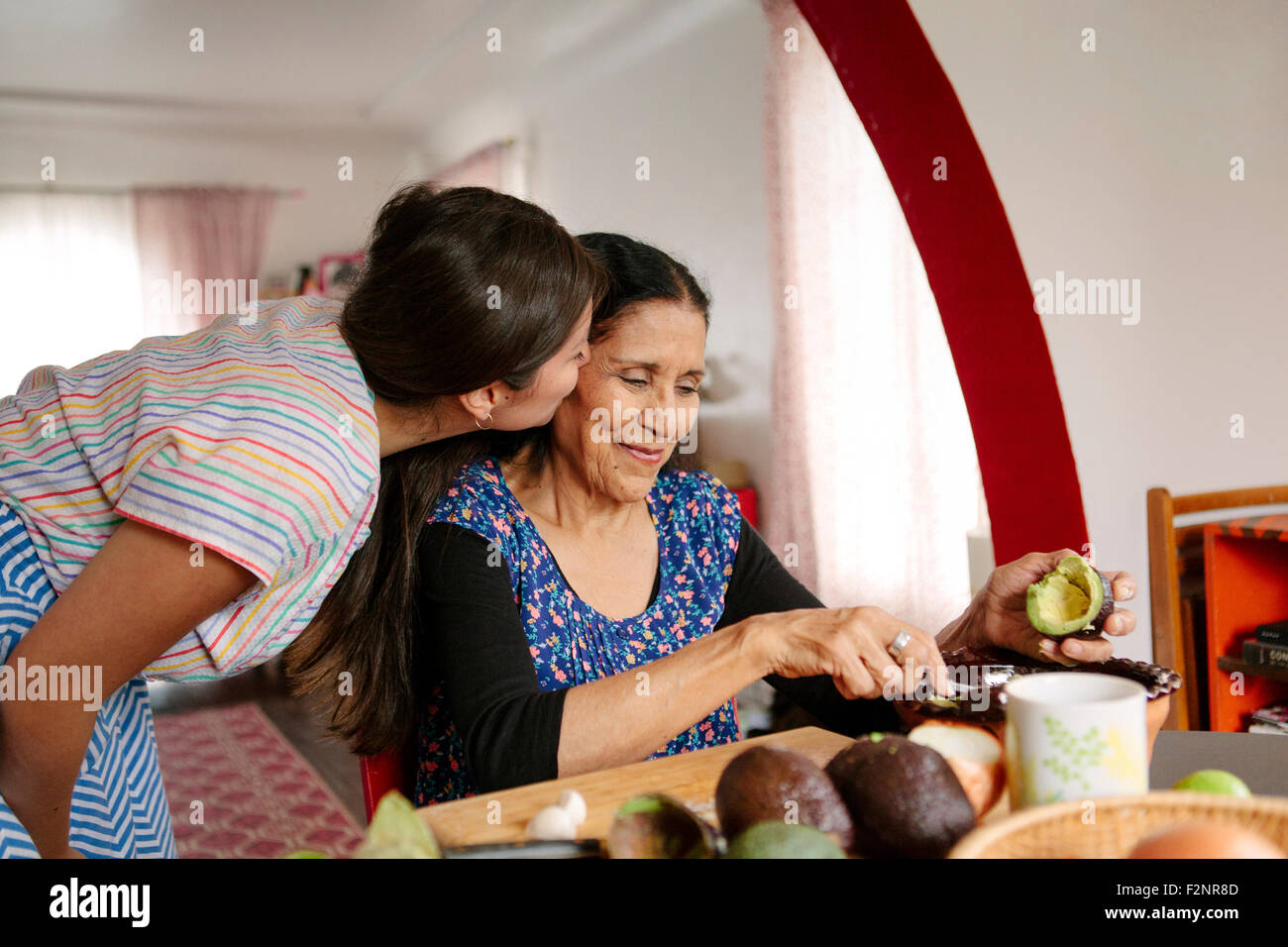 Woman kissing grandmother cooking in kitchen Stock Photo