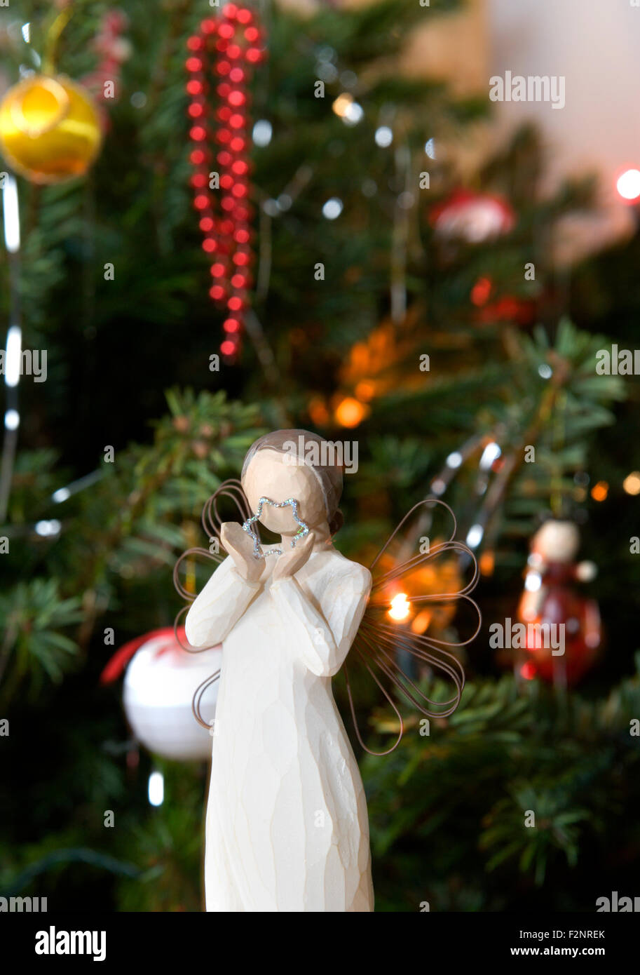 A festive image of an angel holding a star shape in front of a traditional real pine Christmas tree Stock Photo