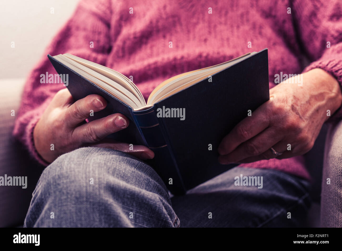 a mature person is sitting in an armchair, reading a book. Stock Photo