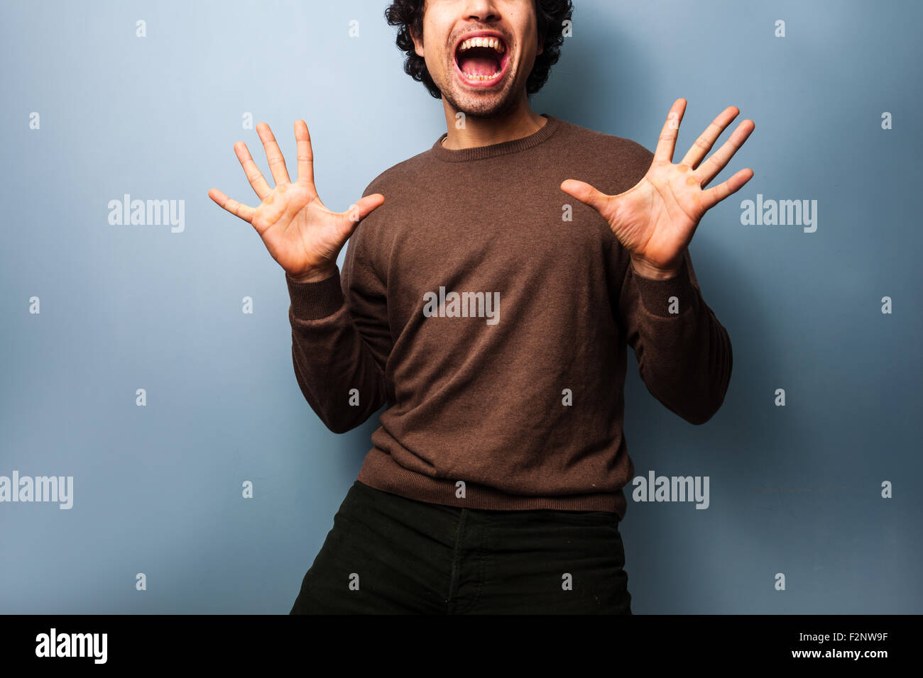 an excited young man holds up his jazz hands, smiling mouth wide open. Stock Photo