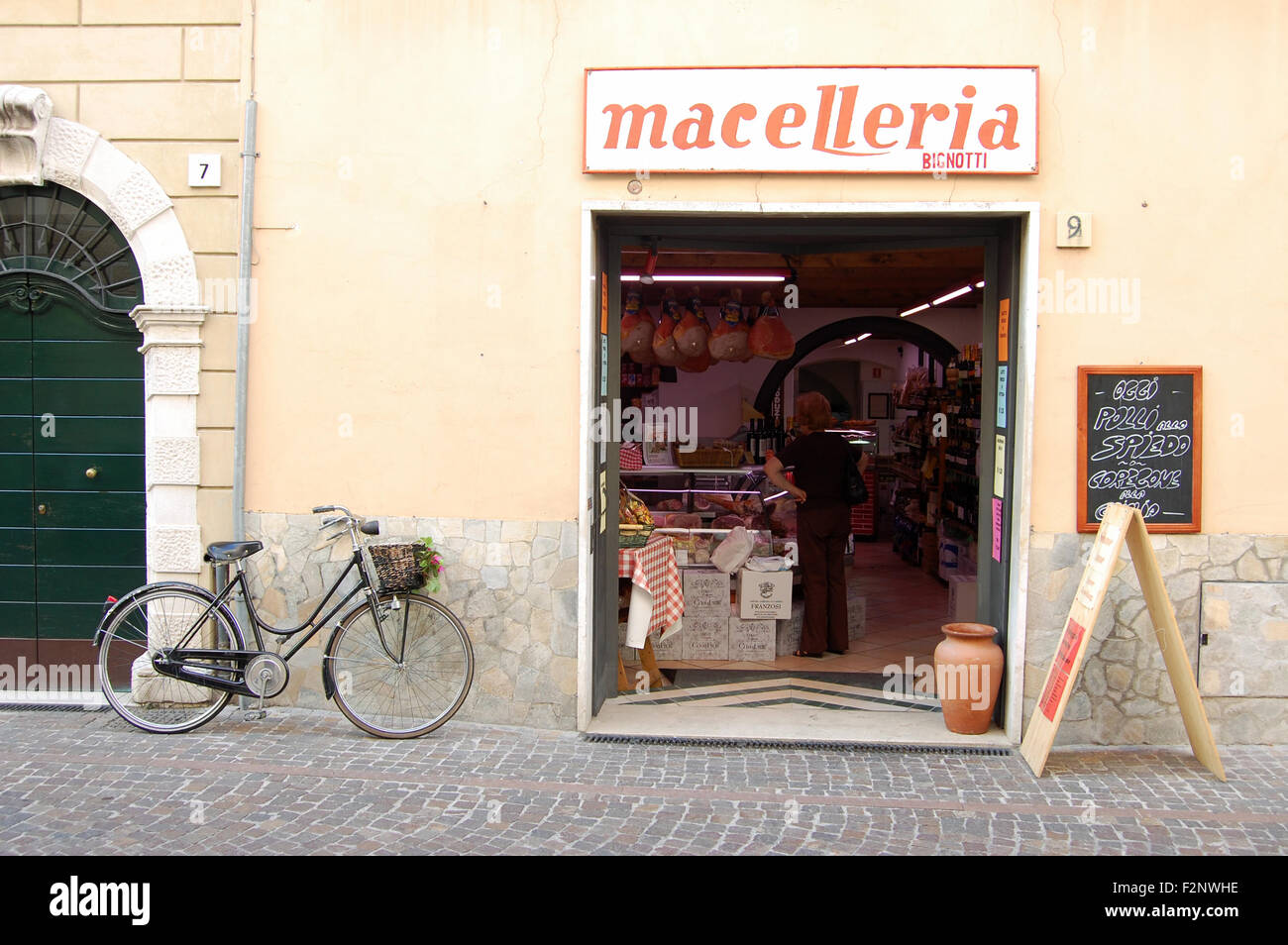 Customer waiting, her bicycle parked outside, in the delicatessen Macelleria in the small town of Gargnano, Lake Garda in Italy Stock Photo