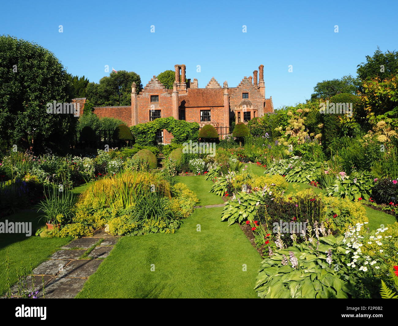 Chenies Manor House and sunken garden with beautiful perennial flower borders and fresh green foliage;sunny with blue sky. Stock Photo