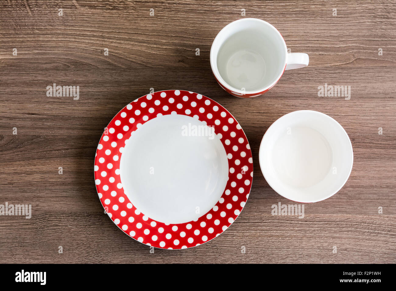 Red polka dotted plate, mug and bowl on brown table Stock Photo