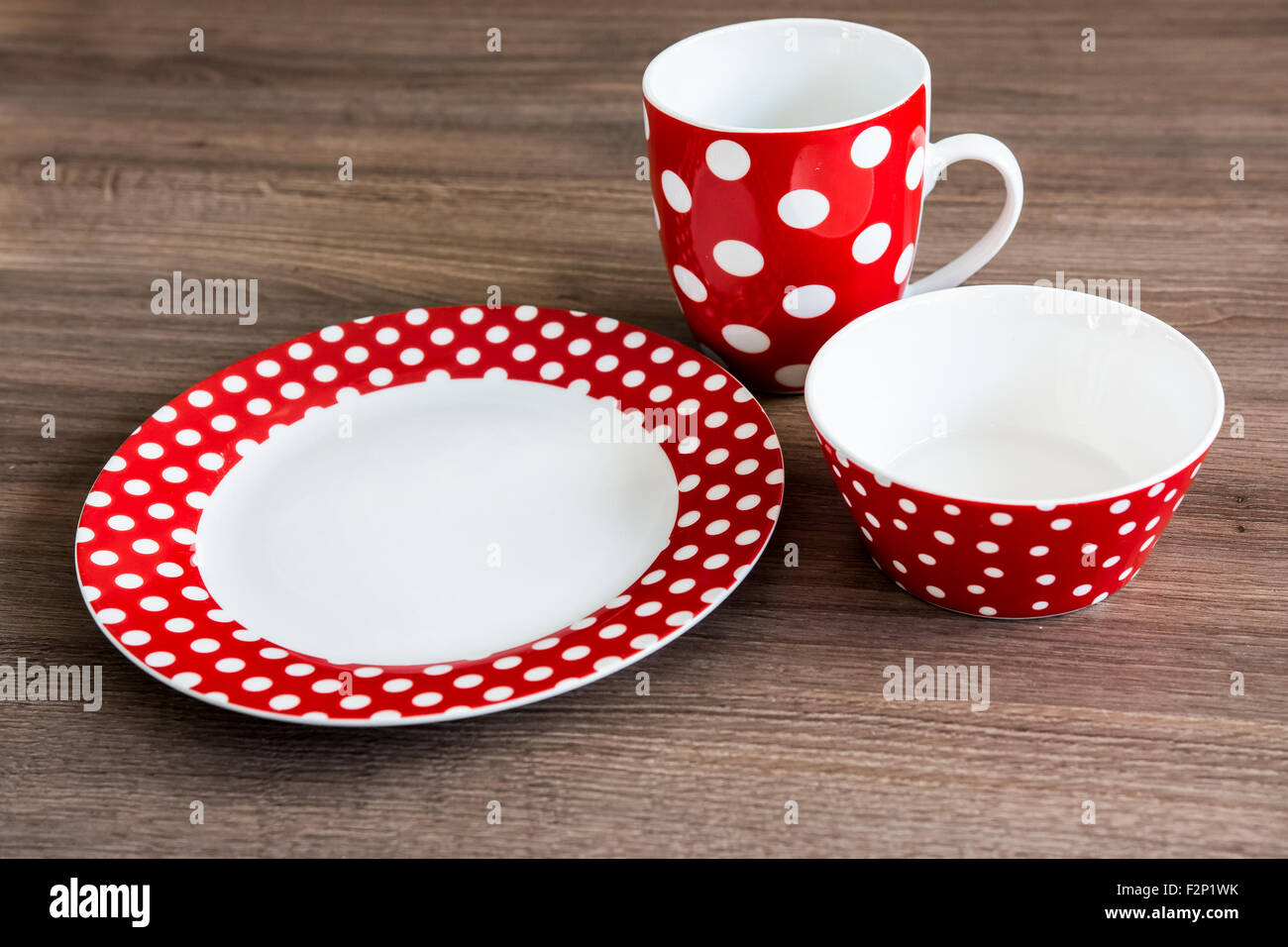 Red polka dotted plate, mug and bowl on brown table Stock Photo