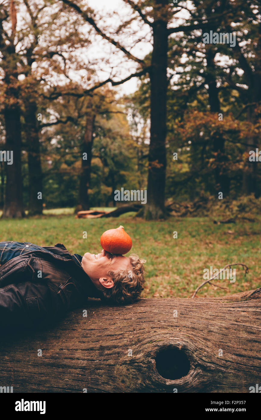 Young man lying on dead wood with a Hokkaido pumpkin on his face in an