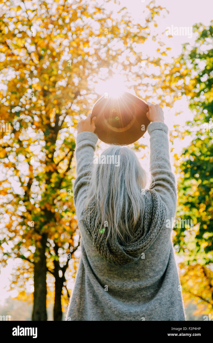 Back view of woman holding hat against the sun in an autumnal park Stock Photo