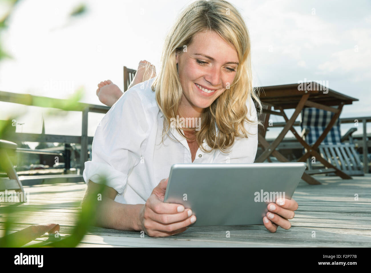 Smiling young woman relaxing on deck using digital tablet Stock Photo