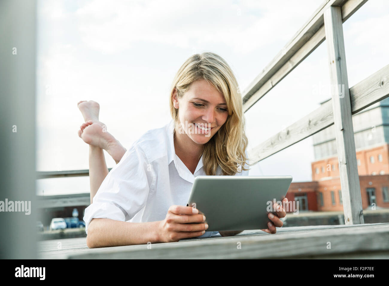 Smiling young woman relaxing on deck using digital tablet Stock Photo