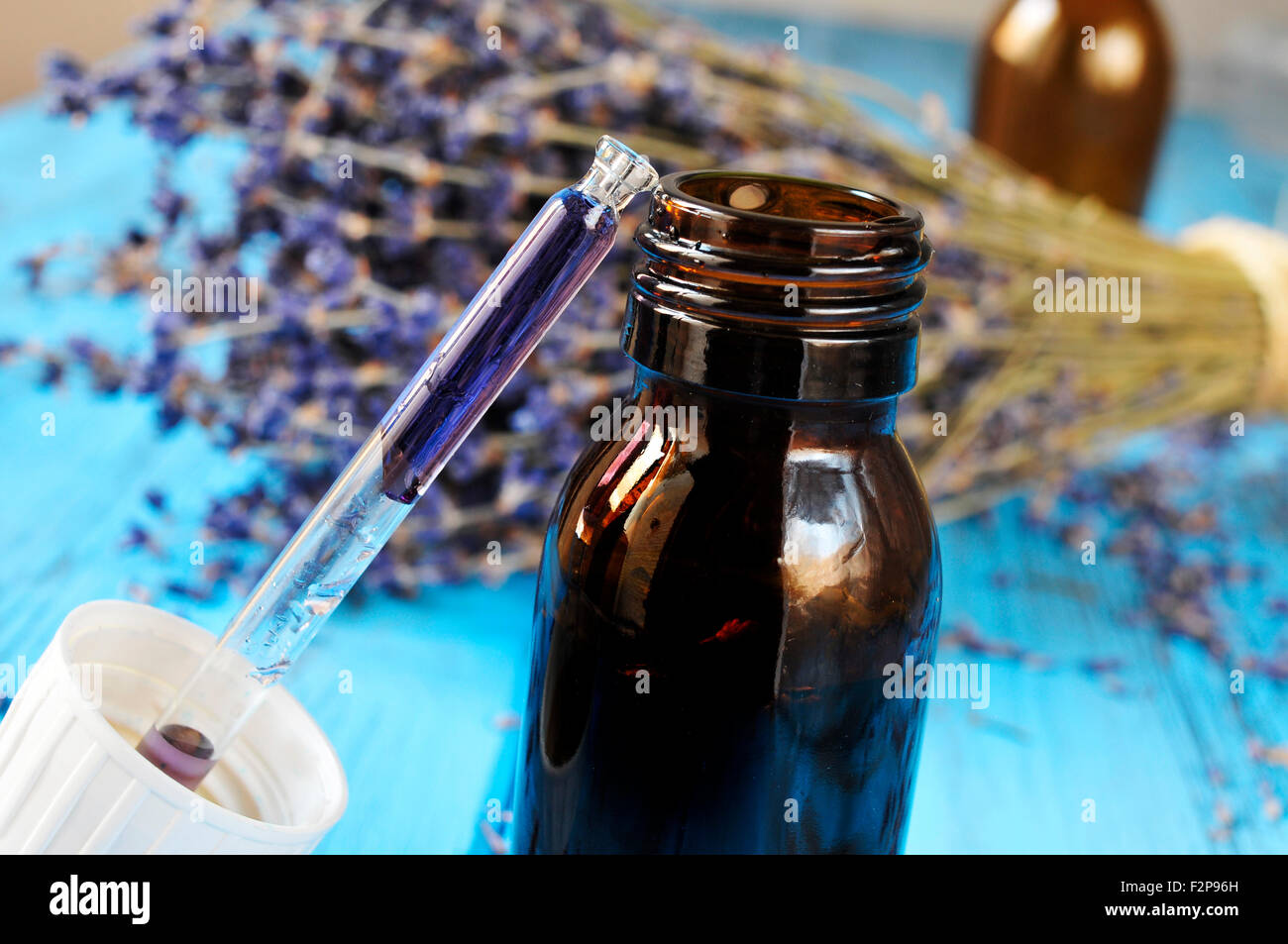 closeup of a dropper bottle with flower essence and a bunch of lavender flowers in the background, on a worn blue wooden surface Stock Photo