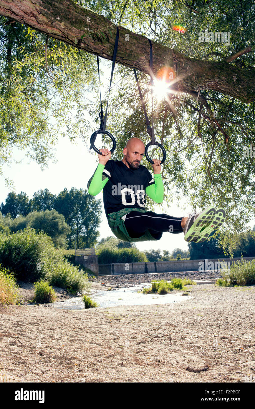 Man doing CrossFit exercise on rings hanging on tree trunk Stock Photo ...