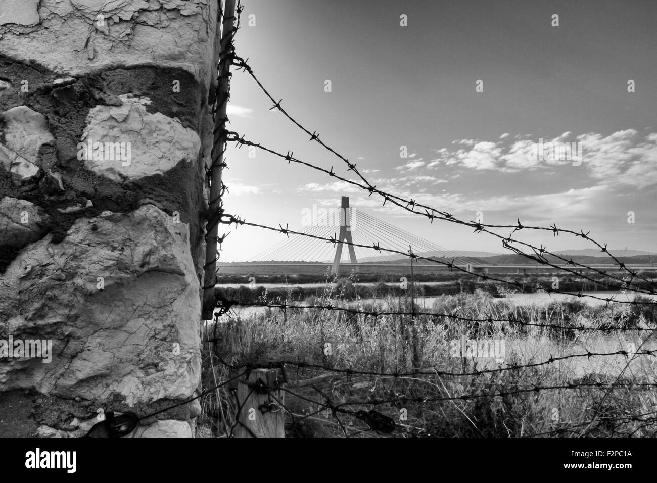BW photo of a stone wall with barb wire with bridge in the back Stock Photo