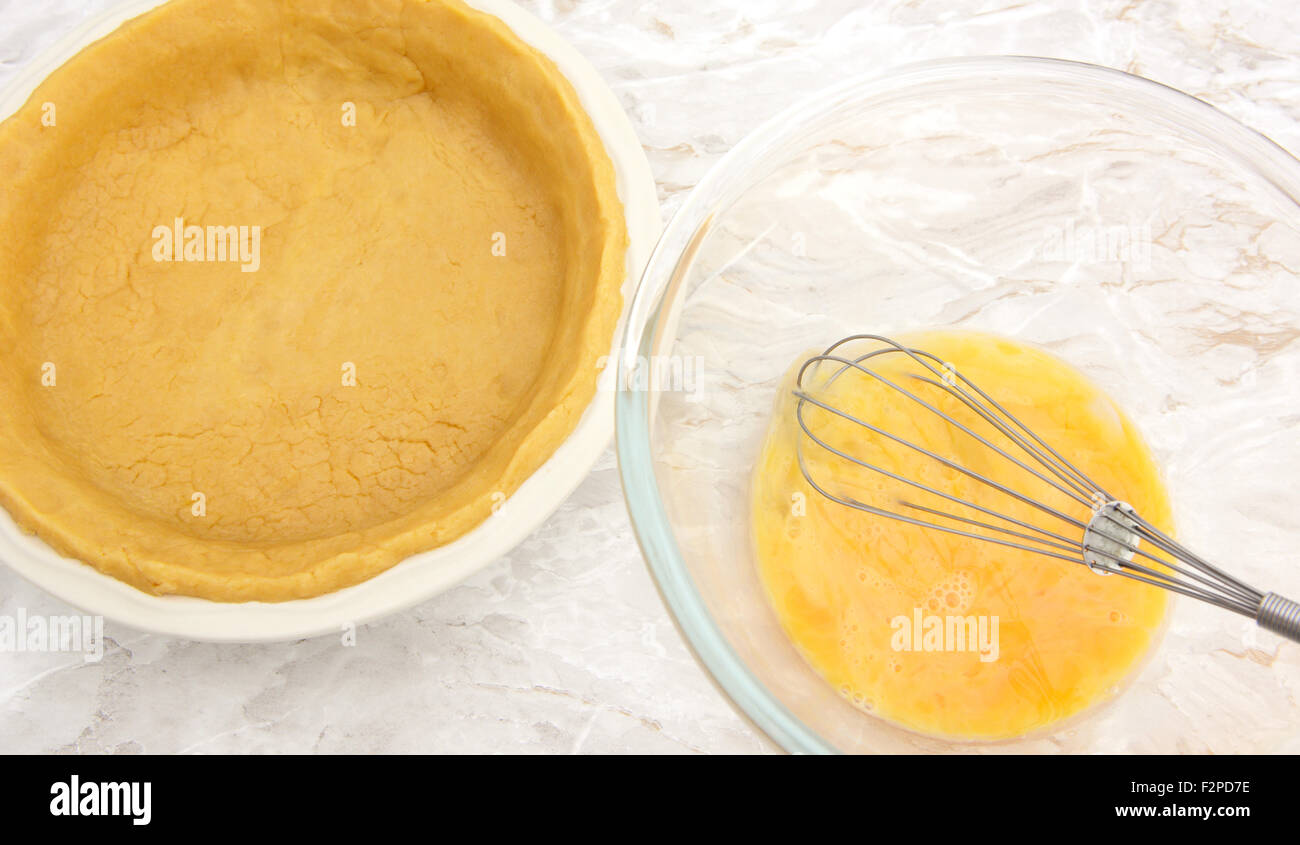 Ceramic pie dish lined with shortcrust pastry next to bowl of beaten