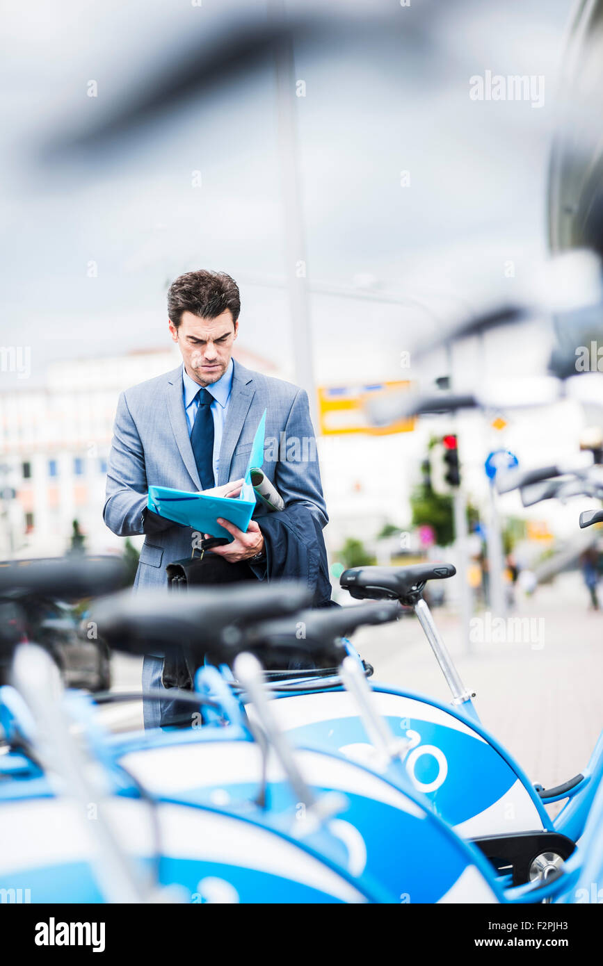 Businessman standing behind rental bikes looking at documents Stock Photo