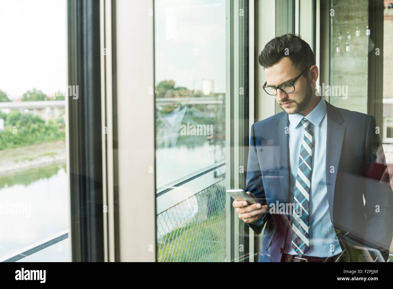 Young businessman at the window looking on cell phone Stock Photo