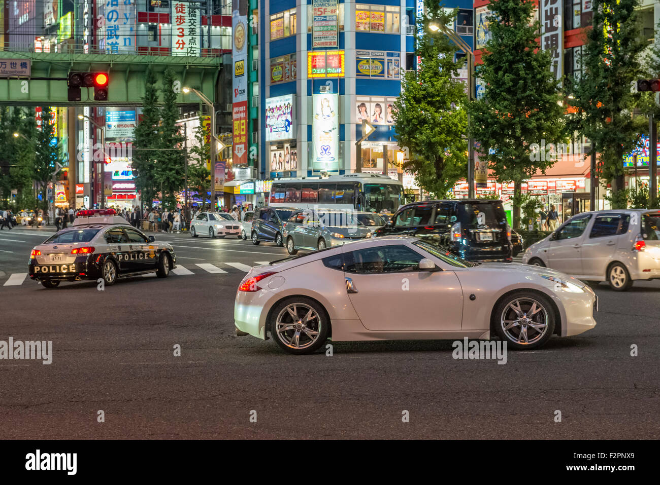 A fast sports car waits to turn with a police car in the background in Akihabara Stock Photo