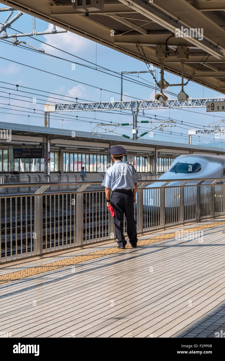 A member of station staff keeping watch on a platform while a Shinkansen bullet train passes Stock Photo