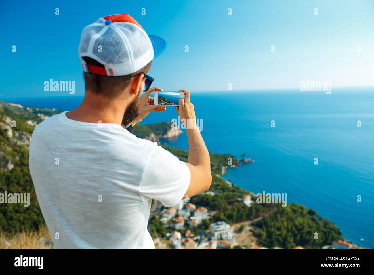 Man makes photos by a smartphone on the background of sea coast, Adriatic sea, Montenegro, Balkans Stock Photo