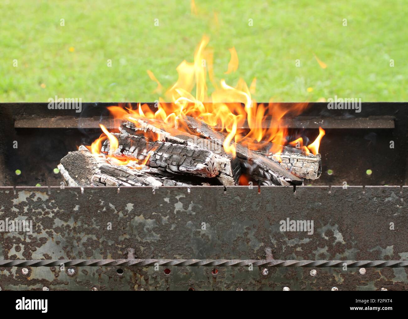 Burning embers in brazier against green grass background Stock Photo