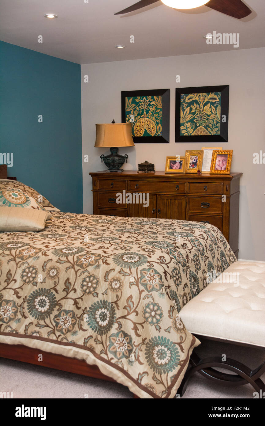 A view of a home's bedroom, including a bed and dresser, with a ceiling fan. Stock Photo
