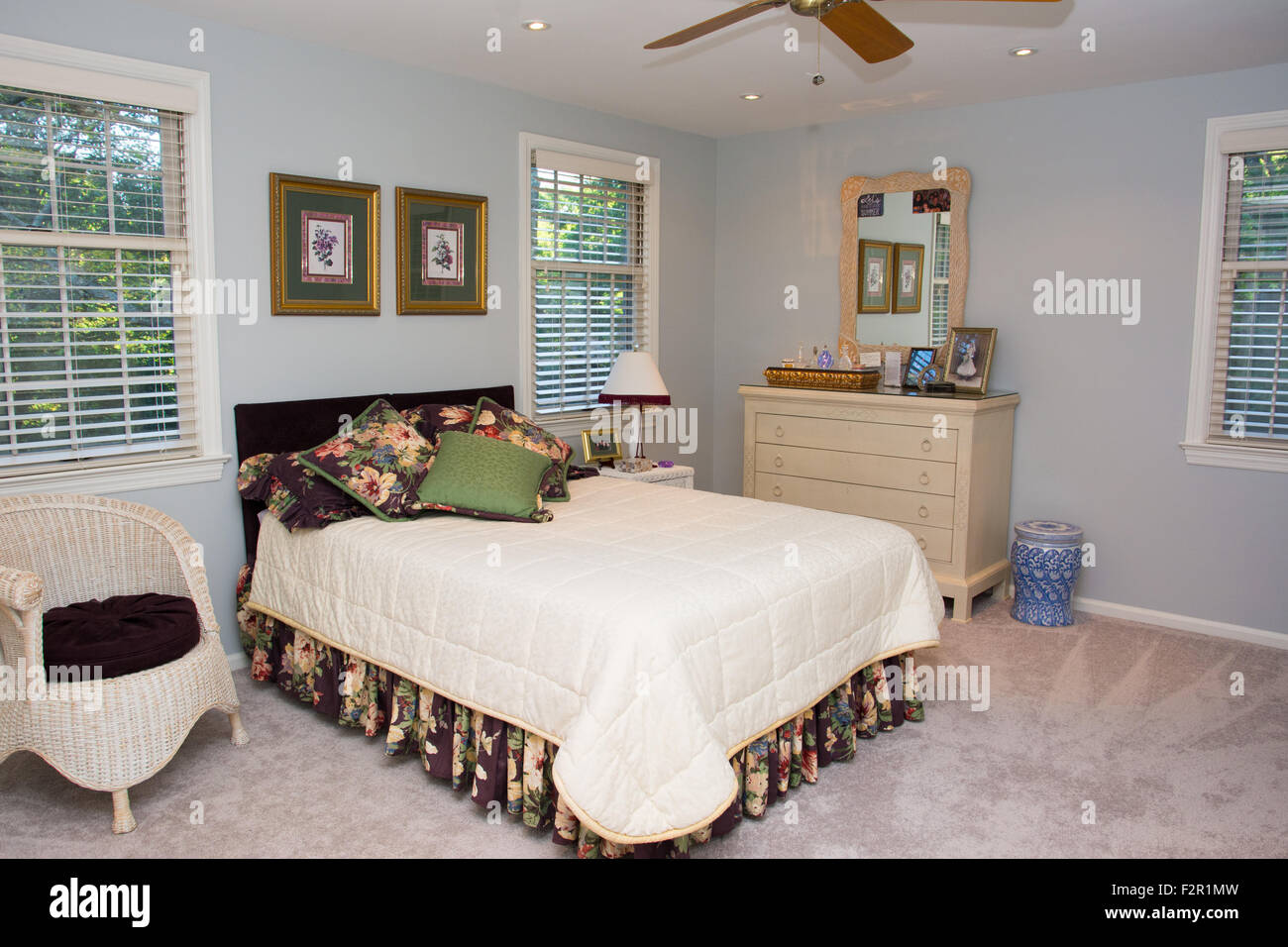 A view of a home's bedroom, including a bed and dresser, with a ceiling fan. Stock Photo