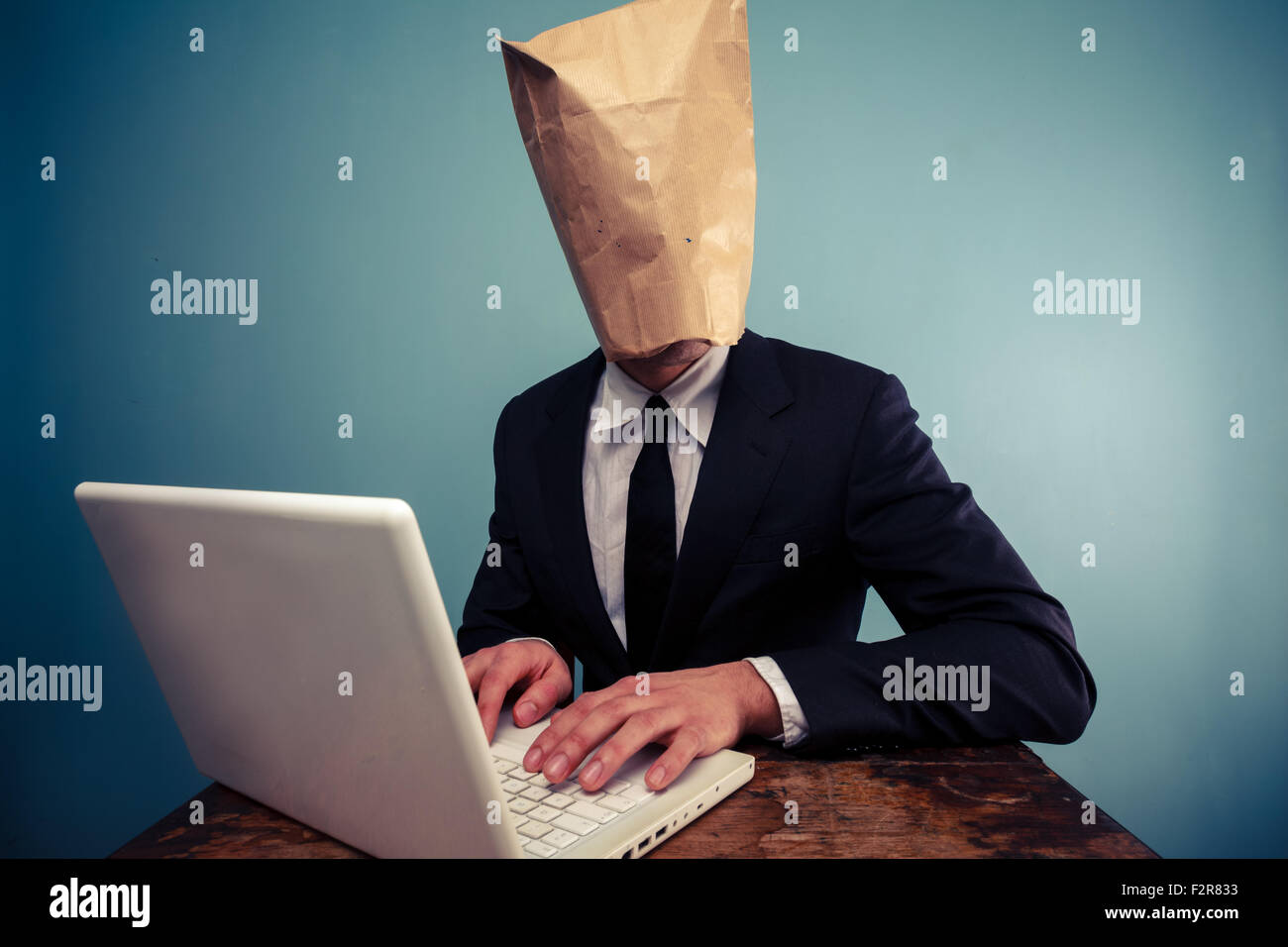 Businessman with paper bag over his head using laptop Stock Photo