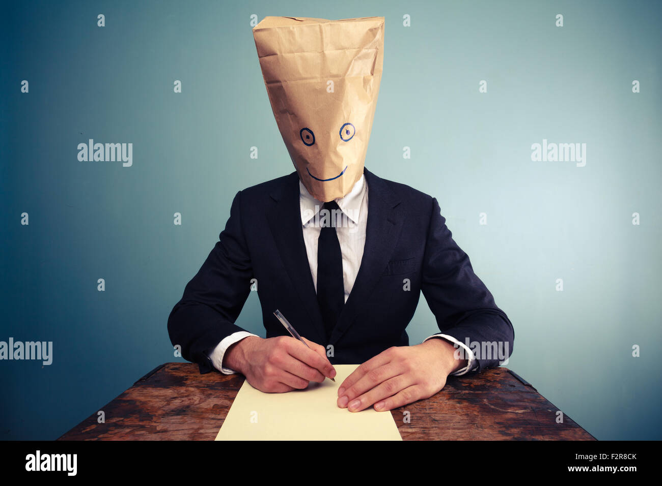 Businessman with paper bag over his head is writing a letter Stock Photo