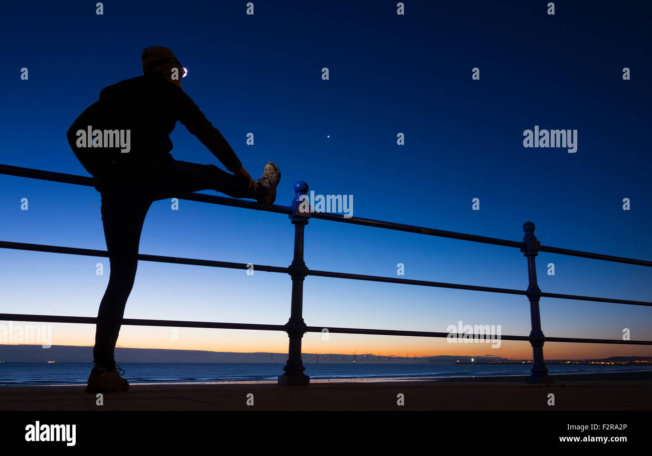 Jogger wearing head torch stretching at sunrise,dawn at Seaton Carew, UK Stock Photo