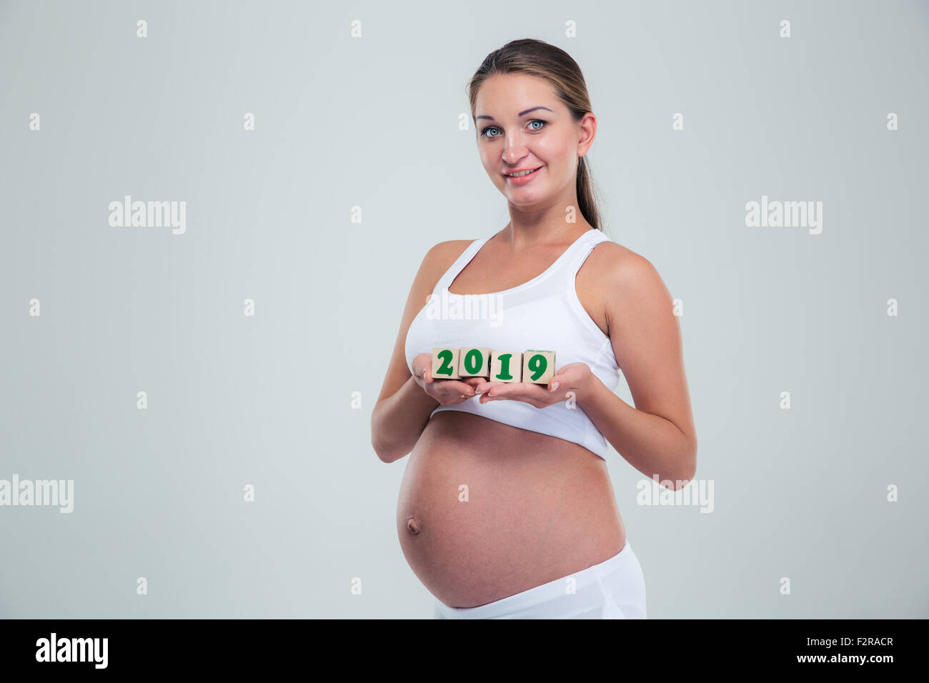 Happy pregnant woman kneeling on the floor in a studio, smiling at her  beautiful baby bump. Young mom-to-be wearing lingerie, cherishing the life  growing inside her with maternal love. stock photo