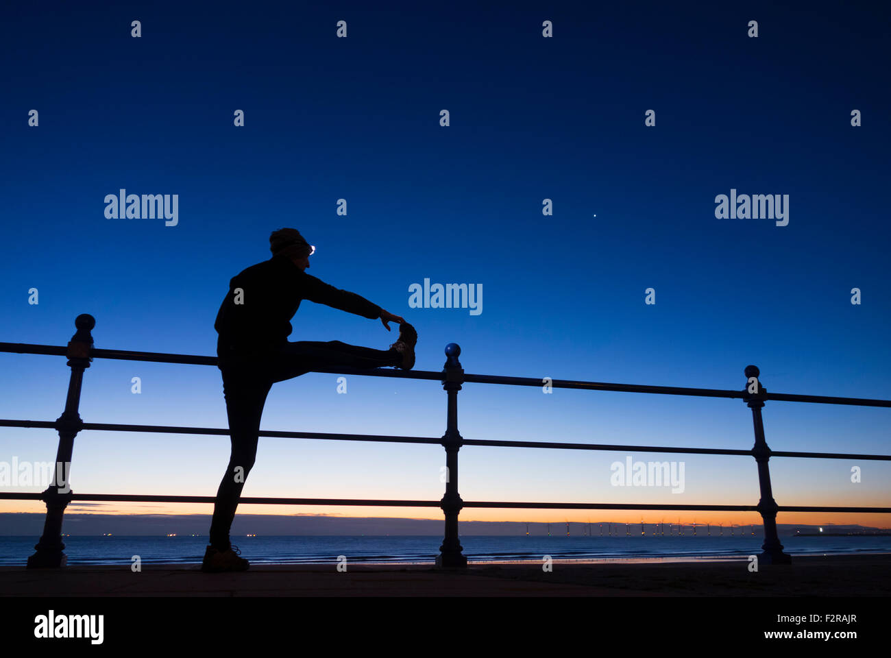 Jogger wearing head torch stretching at sunrise,dawn at Seaton Carew, UK Stock Photo