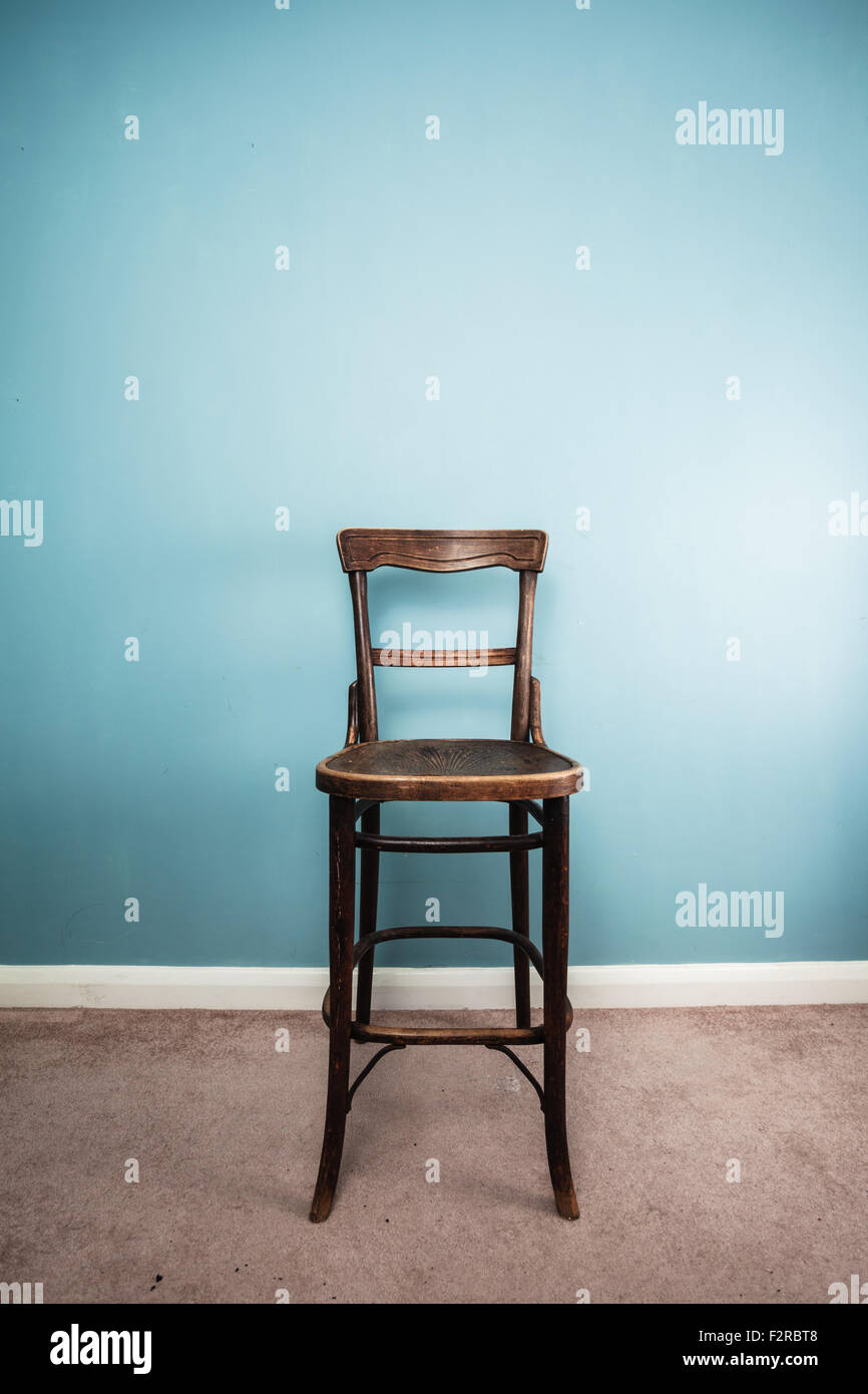 A high, antique wooden chair against a blue wall. Stock Photo