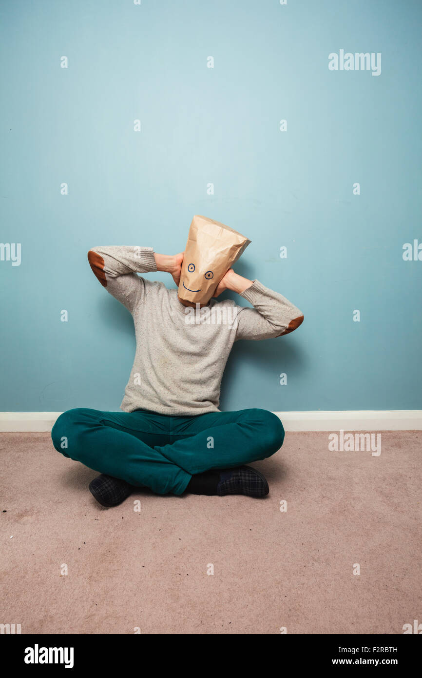 Man with a bag over his head is sitting on the floor and covering his ears Stock Photo