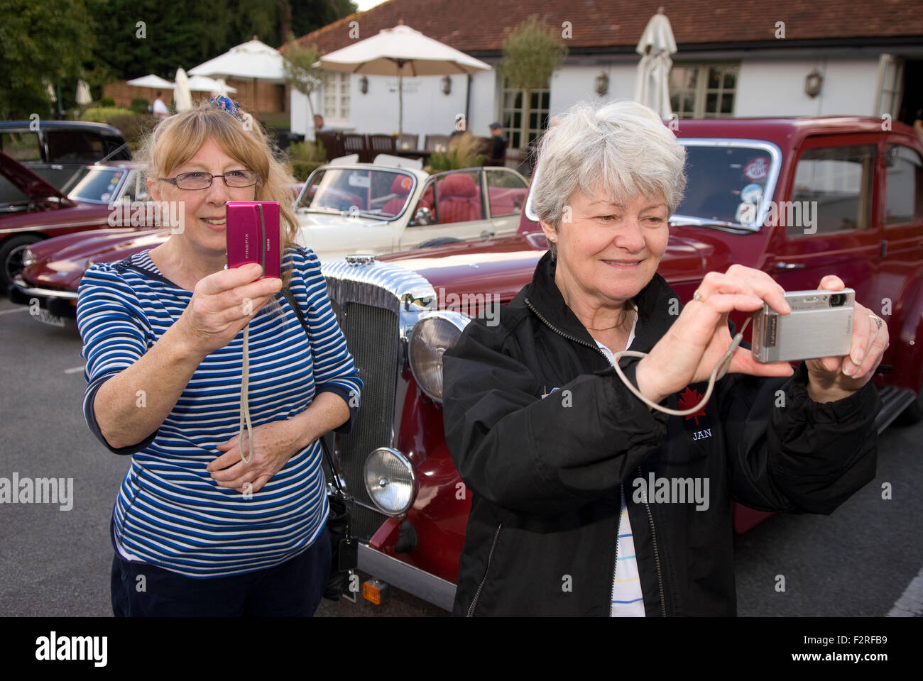 Two elderly women taking photographs at a classic car show, Liphook