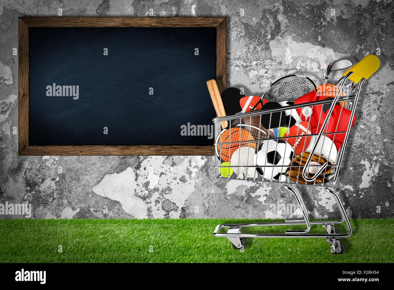 shopping cart filled with sports equipment in front of stone wall with blackboard Stock Photo