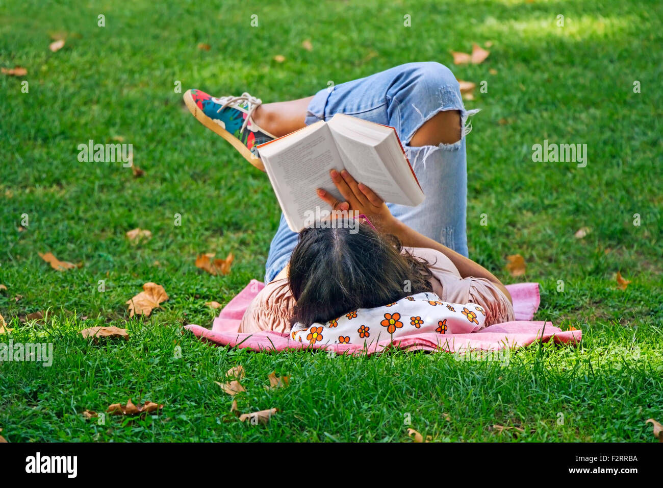 Young girl reading a book lying in the grass in the park Stock Photo
