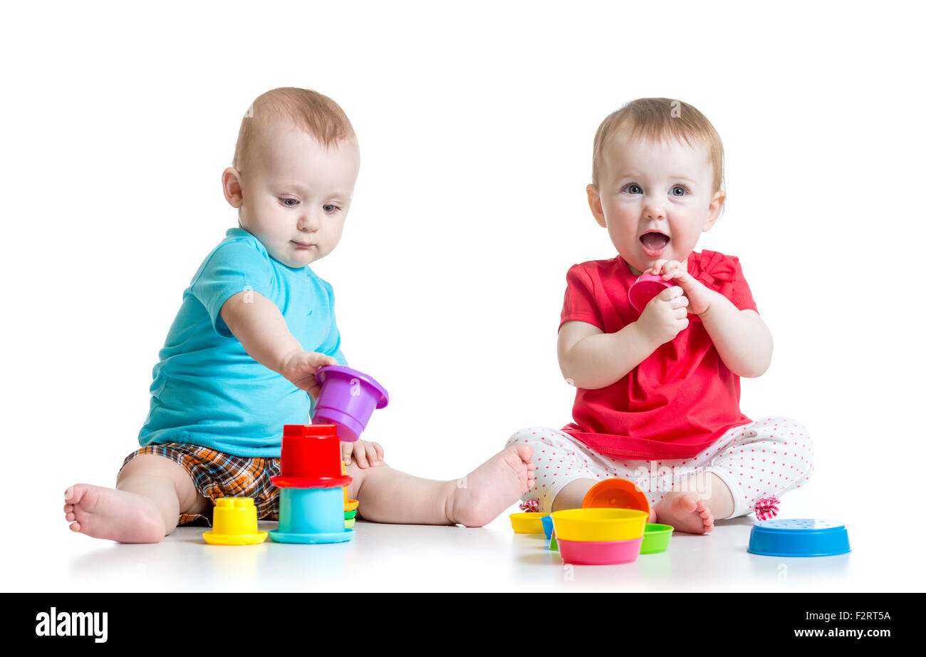 Cute babies playing with color toys. Children girl and boy sitting on floor. Isolated on white background. Stock Photo
