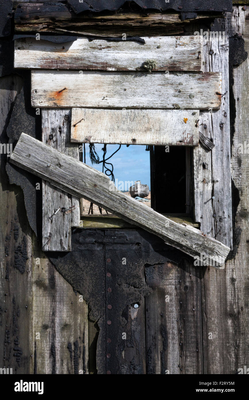 Abandoned fishing boat seen through the boarded window of an old fisherman's shed, Dungeness, Kent, England, UK Stock Photo