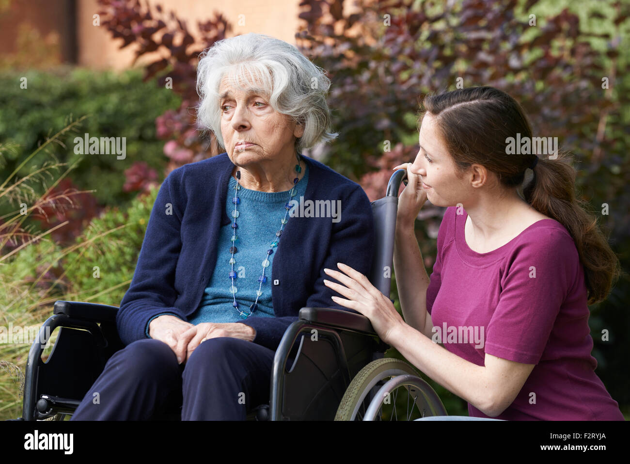 Adult Daughter Comforting Senior Mother In Wheelchair Stock Photo